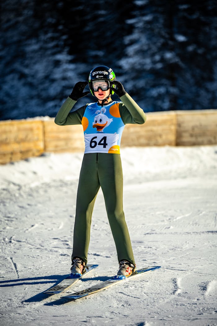 Ski jumper wearing helmet and green suit getting ready on a snowy winter slope.